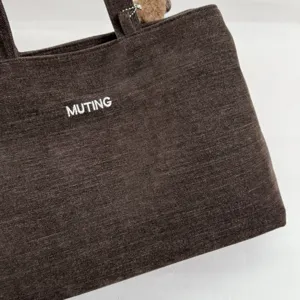 Primer plano de la textura de un bolso marrón oscuro con letras blancas «MUTING» en el frente