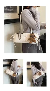 Dettaglio di una borsa bianca a spalla con ciondolo a forma di orsetto e nastri decorativi