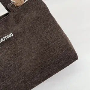 Primer plano de la textura tejida marrón oscuro y el bordado blanco MUTING en el bolso.