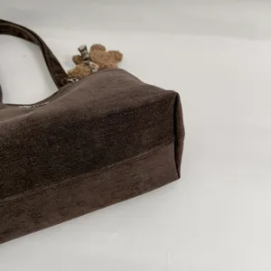 Primer plano de la base de tela marrón oscuro, con costura lateral y pequeño oso de peluche colgante