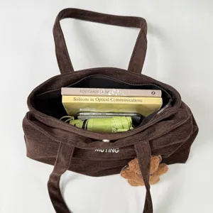 Vista superior de un bolso marrón abierto con libros, móvil, paraguas verde y colgante de osito