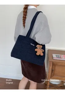 Vista trasera de una modelo con bolso vaquero azul oscuro, bordado MUTING y un osito colgante