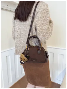 Sac brun en suédine porté à l’épaule par un modèle, avec anses foncées et un pendentif peluche