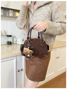 Vue portée d’un sac à main marron en suédine, avec anses foncées et pendentif chat en peluche