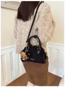 Sac noir porté à l’épaule, avec des détails métalliques dorés et un pendentif ours en peluche