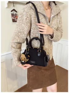 Sac noir effet suédé porté par un modèle, avec ferrures dorées et petit porte-clés chat en peluche