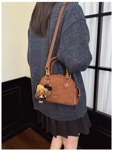 Sac brun à texture effet daim porté sur le côté, avec une longue bandoulière et des détails dorés