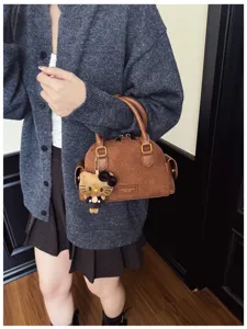 Sac brun à texture suédée, avec des détails dorés et un porte-clés chat en peluche, porté