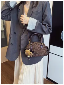 Sac brun à motif léopard avec pendentif chat en peluche, porté avec une veste grise en situation