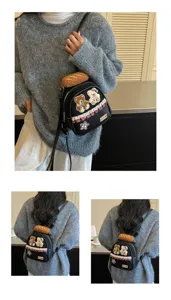 Model wearing a black mini backpack with teddy patches, plaid trim and a plush bread charm
