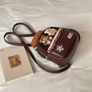 Close-up of a brown faux-leather bag with teddy bear patches, a checkered star and lace trim