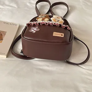 Top-down view of a brown leather-look backpack with teddy bear patches, a plaid star and lace trim