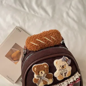 Close-up of teddy bear appliqués, plaid bows and lace trim on the front of a brown textured bag