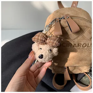 Nahaufnahme eines Plüschbären-Anhängers mit karierter Schleife und Metallclip am Veloursrucksack