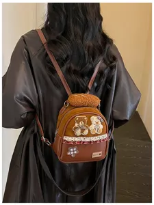 Back view of a brown backpack with teddy bear patches, plaid trim and a plush bun charm