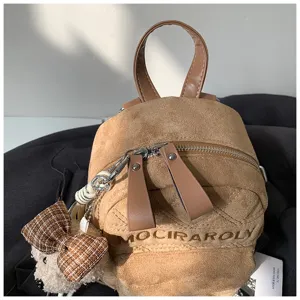 Nahaufnahme eines kleinen Rucksacks aus braunem Velours mit Reißverschluss und Bärenanhänger