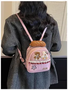 Back view of a person wearing a pink mini backpack with plush bread, bear patches and lace trim