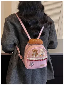 Back view of a pink mini backpack worn over a gray coat, with teddy patches, lace trim and plush top.
