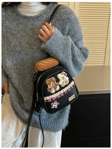 A black mini bag worn over a gray sweater, with teddy bear patches, plaid trim and a star