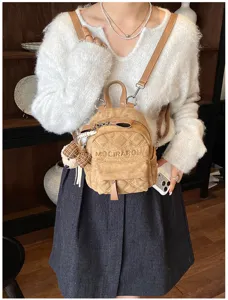 Camelbrauner Rucksack mit Rautensteppung und Teddyanhänger, getragen zum weißen Pullover.