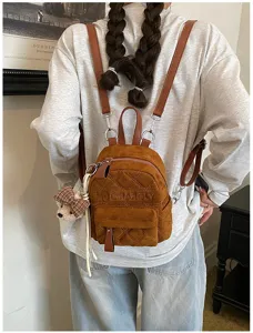 Model mit braunem Wildlederrucksack, Rautensteppung, kariertem Bärenanhänger und Quaste