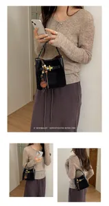 Lifestyle view of a black bucket bag with a woven handle, gold clasp and wooden bead charm