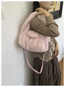 Side view of a model carrying a pink fluffy shoulder bag with a tassel, long strap and bear charm