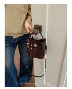 A brown suede and leather bucket bag with a gold buckle and wooden bead tassel, carried by hand