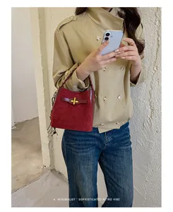 Lifestyle view of a red suede-textured bag with gold clasp and tassels, carried with a beige jacket