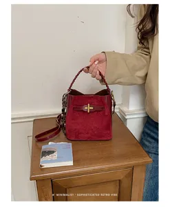 Red suede-texture bag with braided handle and gold clasp displayed on a wooden bedside table