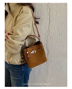 Side view of a model wearing a brown suede-look bag with woven handle and gold clasp