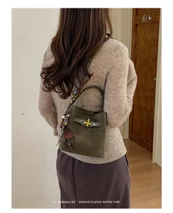 Rear view of a model carrying a green suede-textured bag with woven handle and hanging charms