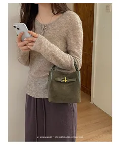 Olive-green bucket bag with woven handle and gold clasp, carried by a model indoors