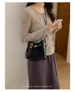 Model wearing a black bucket bag with gold hardware, braided tassels and wooden beads