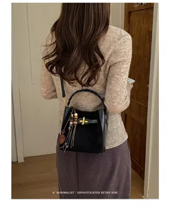 Back view of a woman carrying a black bag with woven handle, gold clasp and wooden bead tassel