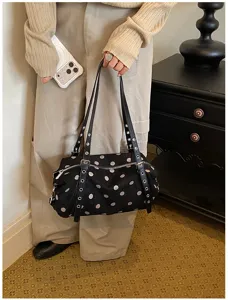 Model holding a black bag with white polka dots, studded shoulder straps and silver hardware