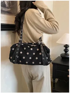 Shoulder view of a black pillow-shaped bag with white dots, studded straps and silver hardware