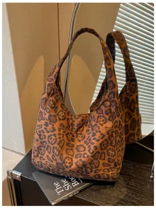 Dettaglio di una borsa morbida maculata, con doppi manici e texture effetto camoscio, su un tavolo