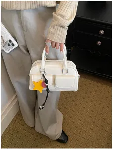 Borsa bianca tenuta in mano, con tasche frontali con patta, due manici e un ciondolo a stella giallo