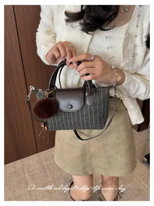 Dettaglio di una borsa in tessuto grigio a righe, con finiture marroni, manici e pompon morbido
