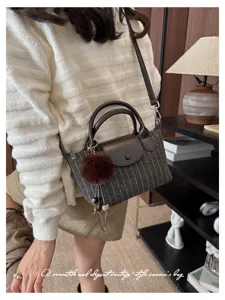 Dettaglio di una borsa a righe grigio antracite, con patta in pelle marrone e pompon morbido