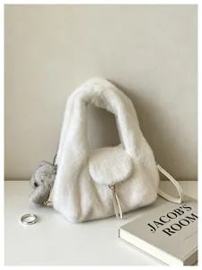 White plush bag with a teddy bear charm and gold-tone chain, displayed beside a book