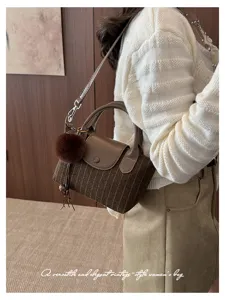 Vista indossata di una borsa a righe marroni con patta in pelle, tracolla e pompon decorativo