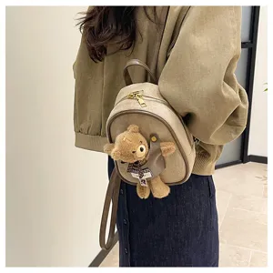 Close-up of a beige suede-look backpack worn with a plush brown bear charm and checked bow