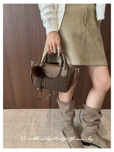 Modella con borsa a righe marroni, patta, pon pon e tracolla a catena, abbinata a stivali
