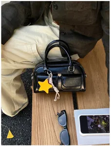 Dettaglio della borsa nera lucida con doppi manici, tasca con zip e ciondolo a stella giallo