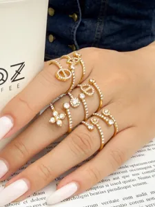 Close-up of a hand wearing stacked gold-tone rings with clear stones in varied decorative shapes