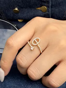 Close-up of a hand wearing a gold open ring with sparkling stones and an oval loop against denim