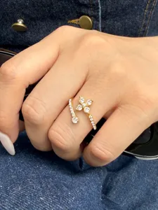 Close-up of a gold-tone open ring with clear stones in a flower-like cluster, worn on a hand