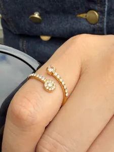 Close-up of an open gold-tone ring with clear stones and floral settings, worn on a finger